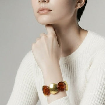 Woman wearing a gold bracelet with amber beads on a neutral background