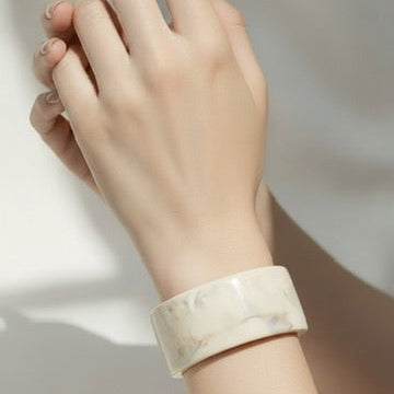 Hand wearing a marble-patterned bracelet on a neutral background