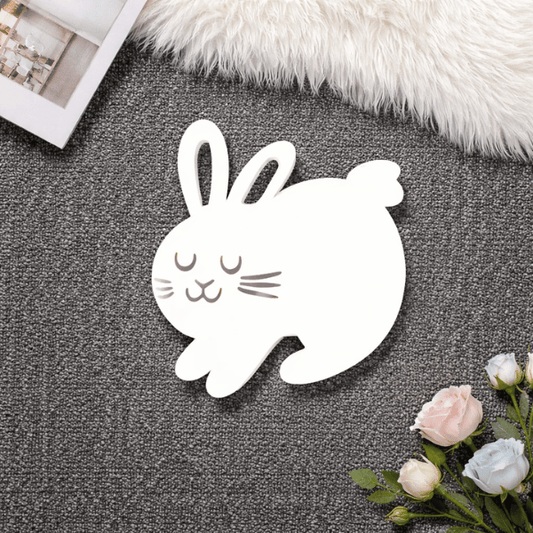 White rabbit-shaped object on a textured surface with flowers and a book in the background