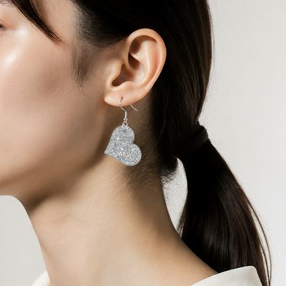 Heart-shaped silver earrings worn by a person with a plain background