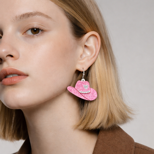 Close-up of a person wearing pink cowboy hat earrings with a neutral background